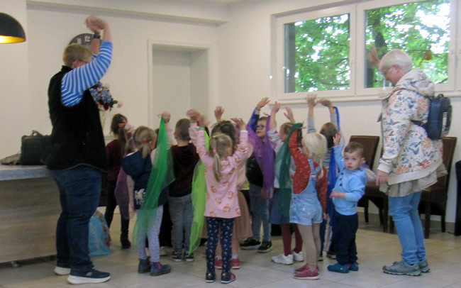 Kinder aus der Kita Arche Noah tanzen mit bunten Tüchern im Seniorenheim