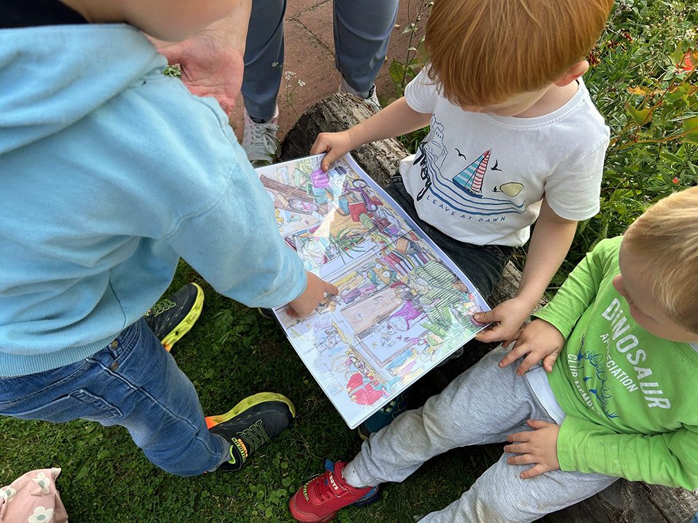 Eine kleine Gruppe von Kindern aus der Kita Retzen sitzt im Freien und liest in einem bunten Bilderbuch.